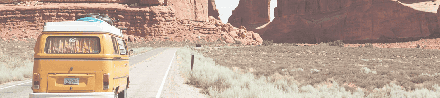 Vintage yellow van driving through a scenic desert landscape with red rock formations.
